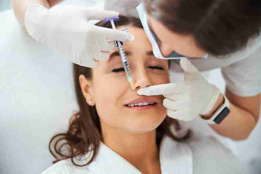 Top view of a dermatologist in a face mask and sterile gloves administering a subcutaneous injection to her patient